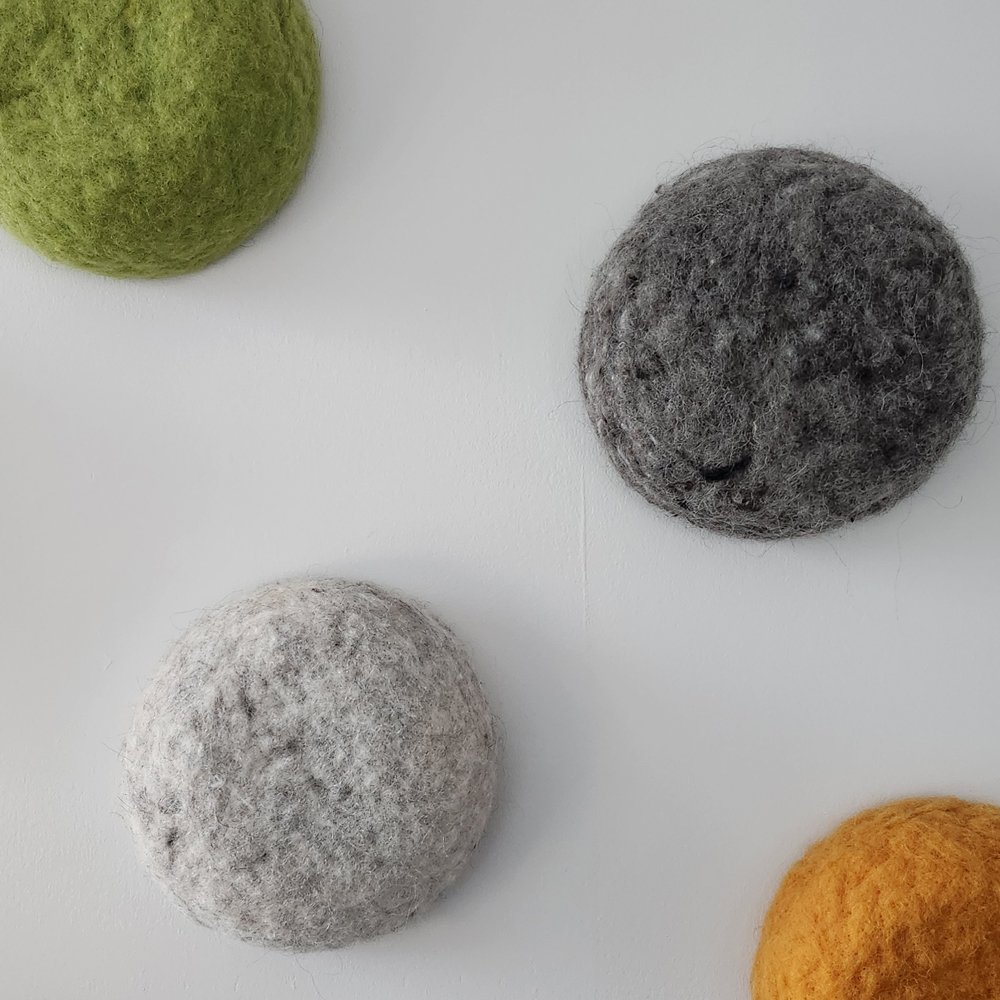 Sjónlýsing á ljósmynd af verkinu Nokkrir kúptir, ullarhnappar á vegg, raðað í skáhallt mynstur. Áferðin er loðin. Hver eining varpar mjúkum skugga niður á vegginn sem leggur áherslu á þrívídd og handverkslega mýkt efnisins.